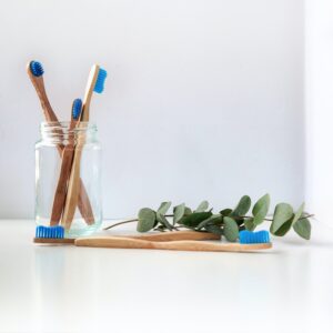 A transparent jar containing 3 wooden toothbrushes and 2 toothbrushes on a the table in front of the jar