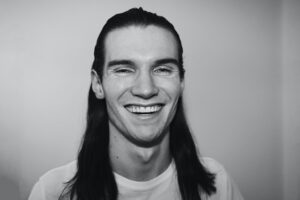 Man with log dark hair smiling, he has white straight teeth, as he invested in braces in Kettering